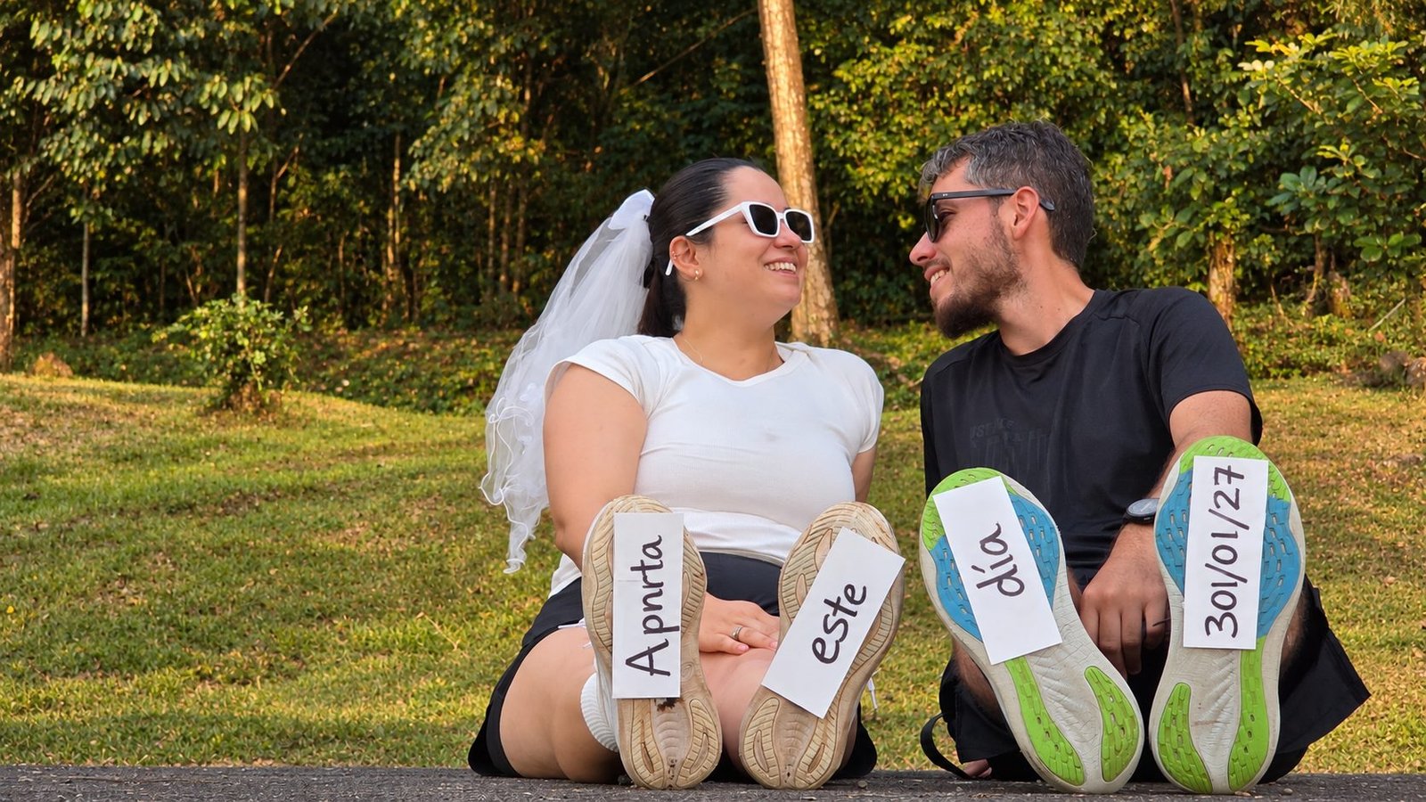 Josafet y Angélica sentados en el césped mostrando las suelas de sus tenis con la fecha de la boda